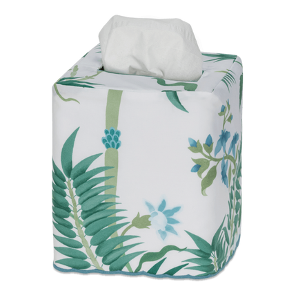 The Matouk Palmyra Tissue Box Cover in Emerald features a green leaf and blue flower pattern, bringing an island-inspired touch to your decor as it neatly covers a square tissue box with a white tissue popping out from the top.