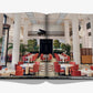 Open book from Assouline featuring The Peninsula London: a Hyde Park hotel with an elegant restaurant, white columns, red chairs, set tables, tall ceilings, and a grand piano on the upper balcony.