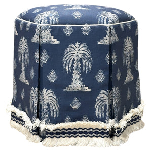 The Highland House Evans Skirted Ottoman showcases a round blue design with white palm tree patterns, finished with white fringe and blue-and-white braid for a stylish, custom look.