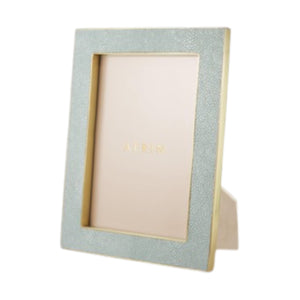 The Classic Shagreen Frame Collection by Aerin features a rectangular, light blue and gold modern classic frame with a stand, shown at an angle with a blank placeholder inside.