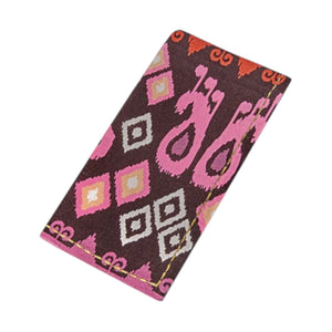 The Dancing Ikat Ganache Collection by Figue features a rectangular textile with a brown base and pink, orange, and white geometric patterns, evoking traditional design and pairing beautifully with any cotton linen dining décor.