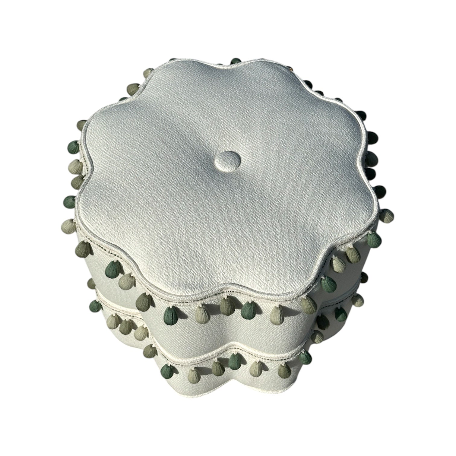 The Stella Stool with Trim by Bunny Williams features textured white scalloped upholstery, a centered button, and green and gray pom-pom edging. This charming stool doubles as a stylish ottoman or footrest, shown against a white background.