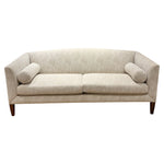 The Ferrell Mittman Norman Sofa in Tinto features elegant beige upholstery, two seat cushions, cylindrical bolsters, angled arms, and wooden legs.