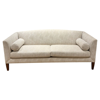 The Ferrell Mittman Norman Sofa in Tinto features elegant beige upholstery, two seat cushions, cylindrical bolsters, angled arms, and wooden legs.