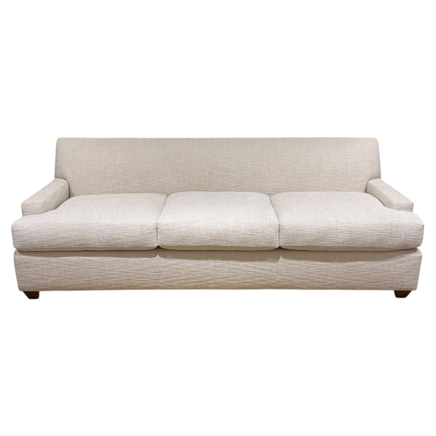 The Baker Yves Sofa is a beige, three-cushion luxury piece featuring a low backrest and armrests, upholstered in textured fabric and shown against a white background.