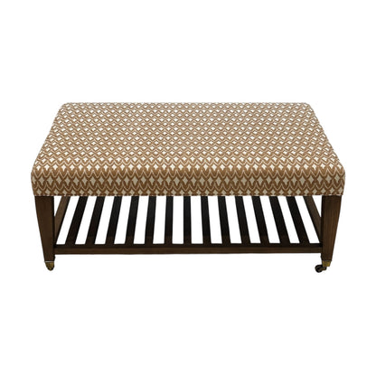 The Lee Industries Upholstered Cocktail Ottoman features a brown and white arrowhead-patterned cushion, wooden legs, a slatted lower shelf, and small wheels on one side.