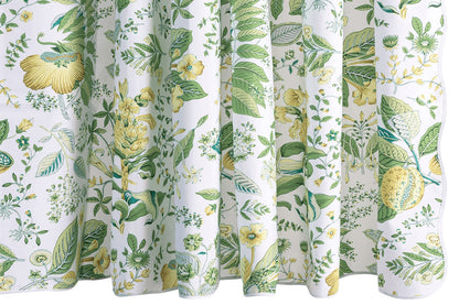 The Pomegranate Shower Curtain Collection by Matouk showcases a white backdrop adorned with green and yellow botanical prints of assorted leaves, flowers, and plants in a detailed, symmetrical design—crafted from luxurious Luca percale and inspired by Schumacher’s iconic botanical motifs.