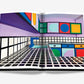 An open book displaying a colorful, geometric interior design with various shapes and patterns in vibrant hues. The room, reminiscent of 1960s and ’70s Pop Art Style, features checkerboard and grid motifs on the floor and walls. The book is "Pop Art Style" by Assouline.