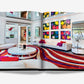 An open magazine displays a colorful living room with vibrant Pop Art Style artwork by Assouline, white sofas with pink pillows, and a red striped rug. Two mirrors hang on the walls.