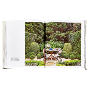 An open spread of The Principles of Pretty Rooms by Graphic Image shows a formal garden with a round table and two chairs—an inspiring scene for interior designers seeking timeless interiors and beautiful color palettes.