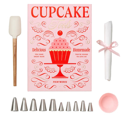 The Essentials Cupcake Tools by PrintWorks includes a spatula, recipe booklet, piping tips, a rolled cloth with a pink ribbon, and a pink cupcake liner—all stylishly displayed on a white background.