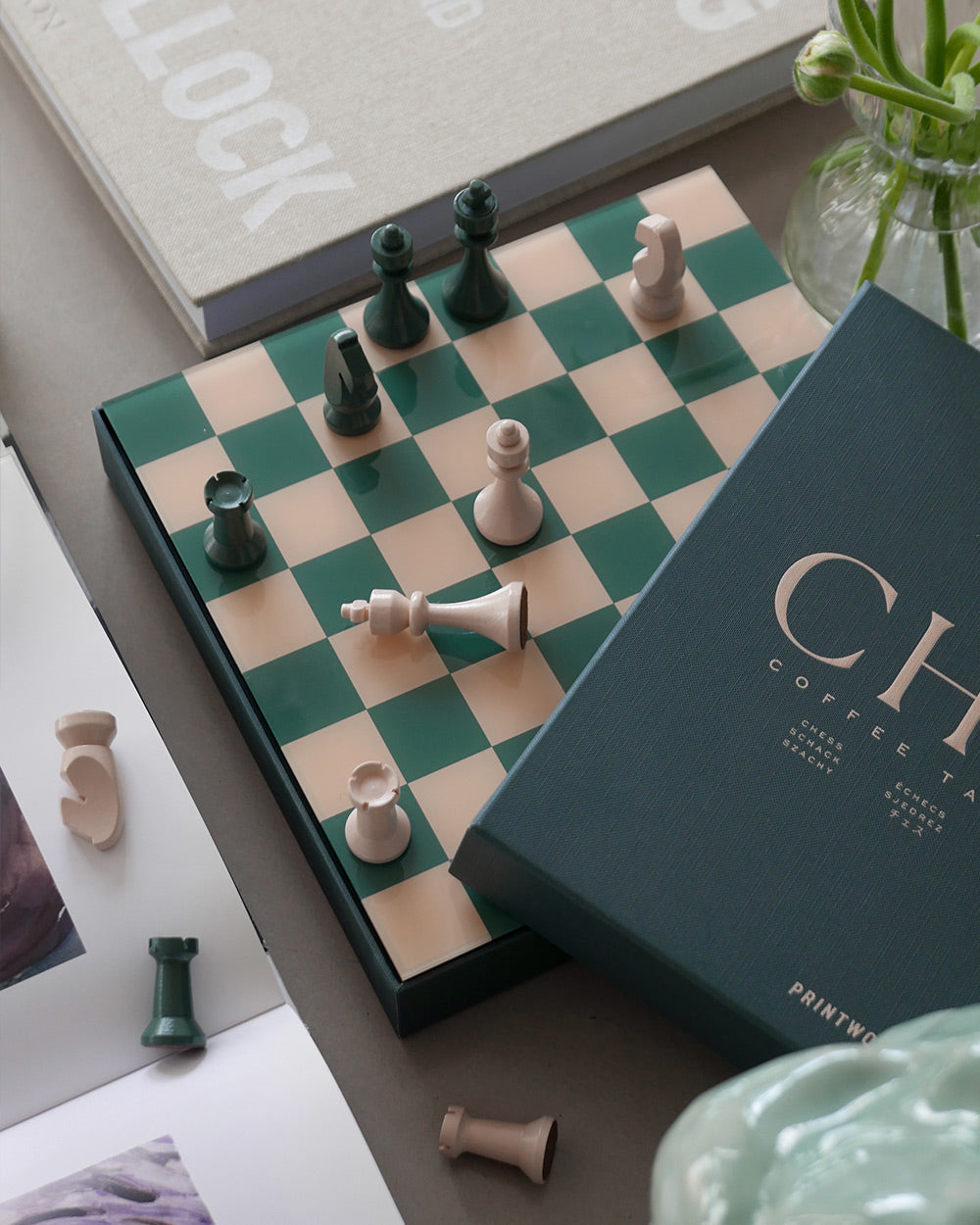 The PrintWorks Chess Collection features a green and beige chessboard with scattered pieces, set among books and décor—an elegant choice for lovers of classic board games.