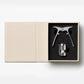 An open beige box from PrintWorks displays The Essentials Champagne Tools—a metal opener and bottle stopper set in black foam, perfect for any champagne kit.