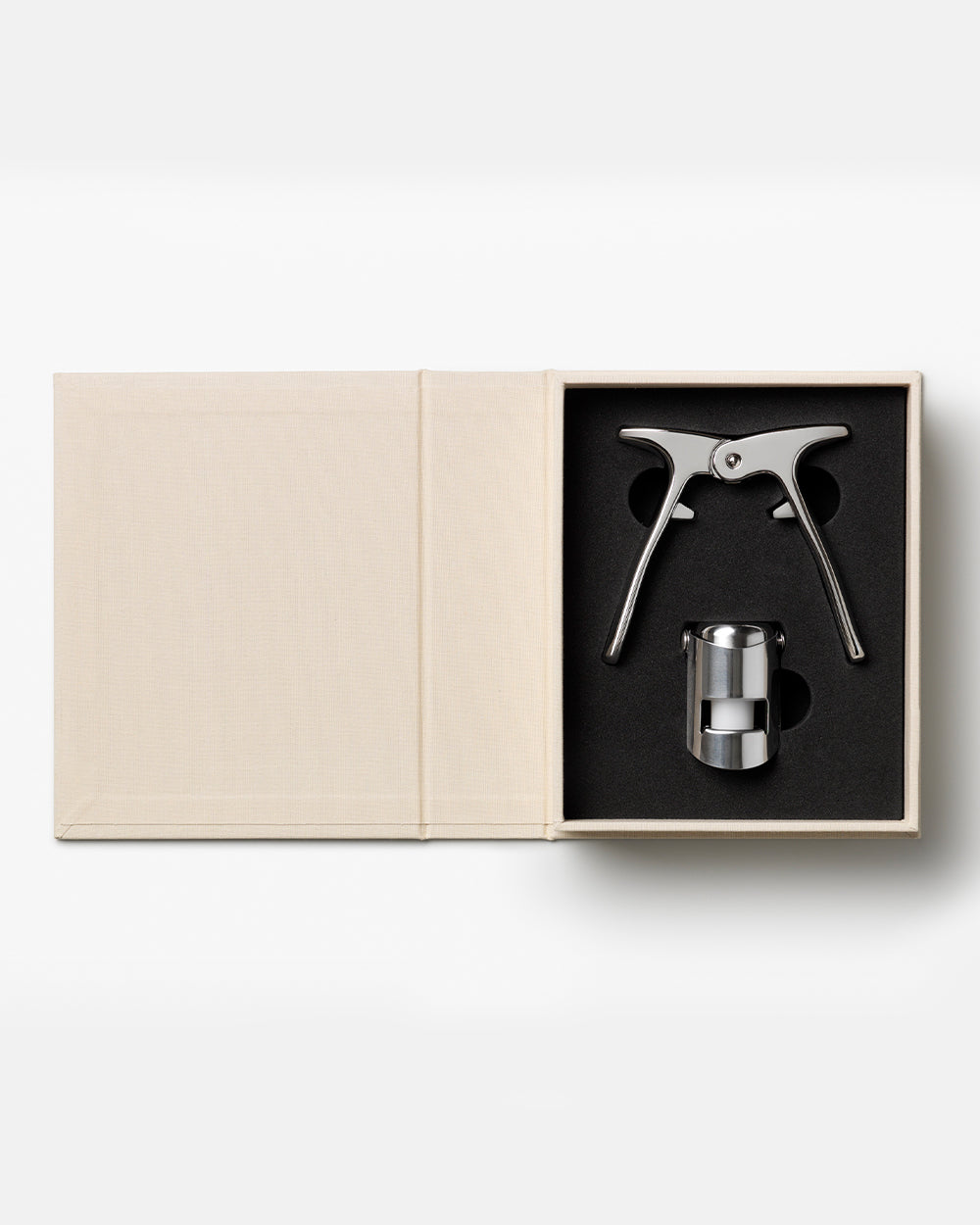An open beige box from PrintWorks displays The Essentials Champagne Tools—a metal opener and bottle stopper set in black foam, perfect for any champagne kit.