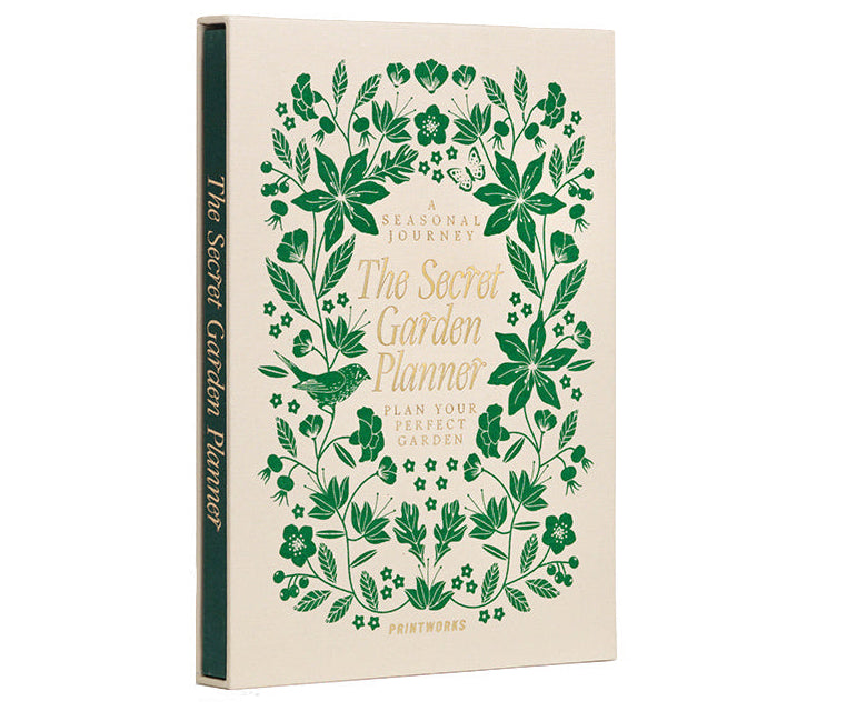 The PrintWorks Secret Garden Journal is a hardcover gardening planner with green floral designs on a beige cover, shown upright and slightly angled left. Ideal as a plant tracker or garden journal.