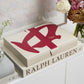 The PrintWorks Mahjong Reverra Game Set, featuring a bold red abstract design, rests on a Ralph Lauren book and is surrounded by vases of flowers atop a white cabinet.
