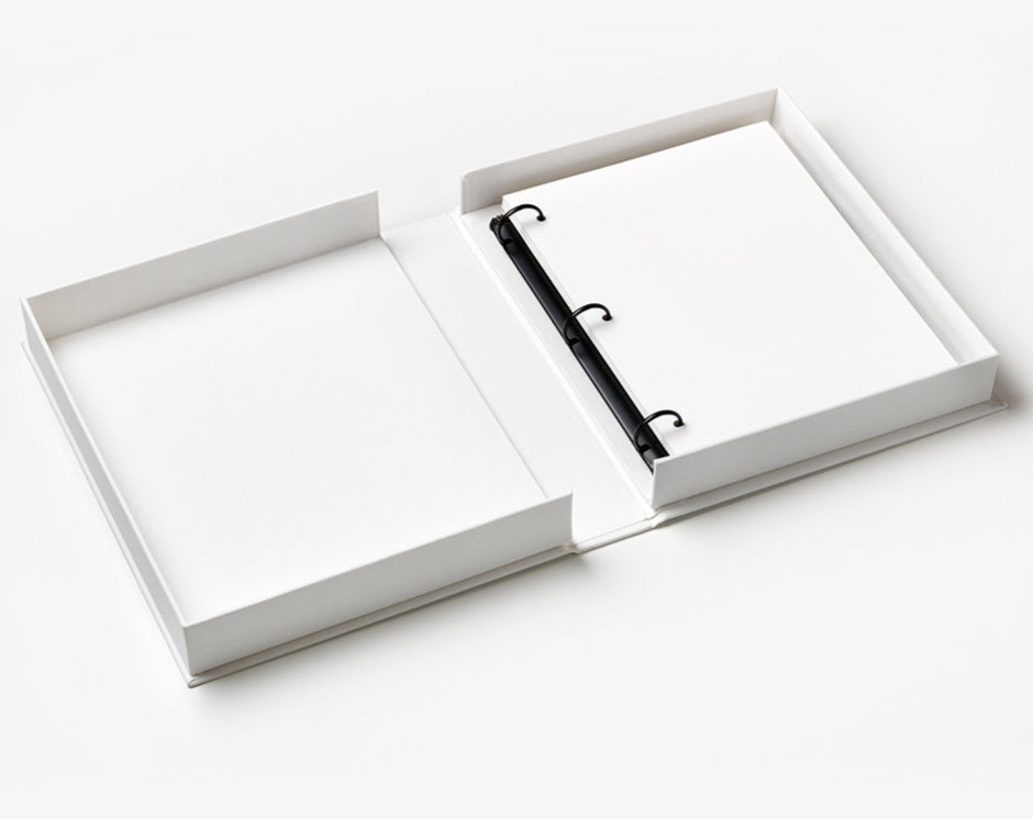 A Dream Big Little One Photo Album by PrintWorks, styled like a baby milestone book, lies open with its white cover fully extended on a flat surface, displaying blank pages held by three rings.