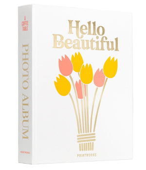 The PrintWorks Hello Beautiful Photo Album features a white cloth cover with “Hello Beautiful” in gold, yellow and pink tulips, and “PHOTO ALBUM” on the spine—ideal for your coffee table or as charming home decor.