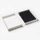 Open white box showcasing the PrintWorks Hello Beautiful Photo Album—a black ring-bound notebook with a white cloth cover on the right and an empty compartment on the left—ideal as a chic coffee table album or stylish home decor.
