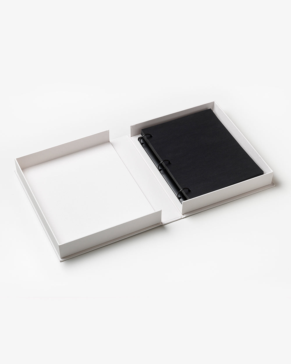 Open white box showcasing the PrintWorks Hello Beautiful Photo Album—a black ring-bound notebook with a white cloth cover on the right and an empty compartment on the left—ideal as a chic coffee table album or stylish home decor.