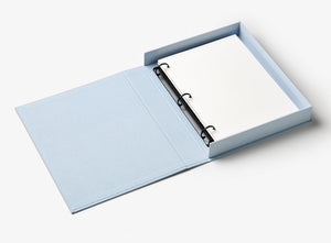 The Perfect Day Wedding Photo Album by PrintWorks, with its light blue cloth cover, lies open like a three-ring binder to reveal blank white pages inside.
