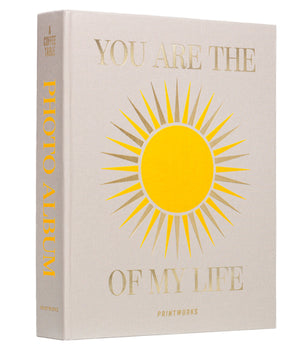 The PrintWorks "You Are The Sunshine Of My Life" photo album features beige covers with gold text and a sun illustration—an elegant coffee table piece that adds charm to your home decor.