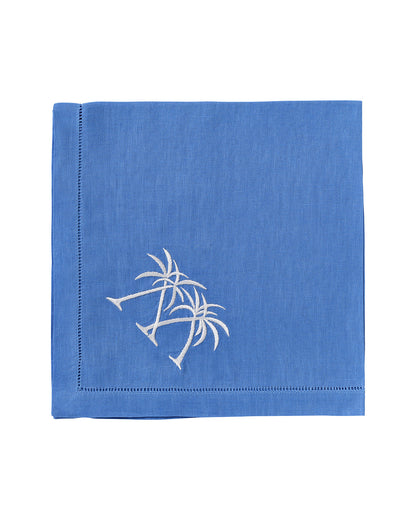 The Pink House Mustique Dinner Napkin Set features square blue linen napkins with white embroidered twin palm trees in one corner—an ideal addition to any luxury table linens collection.