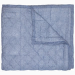 The Nandi Bedding Collection by John Robshaw is displayed partially folded back, highlighting its blue and white pinstriped design on both sides and showcasing the artisanal detail of hand-quilted craftsmanship.