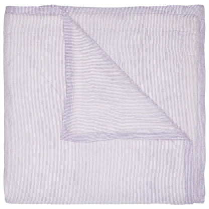 The John Robshaw Nandi Lavender Coverlet features a folded, light lavender hue with subtle vertical stripes, and one corner flipped to reveal its block-printed cotton voile underside.