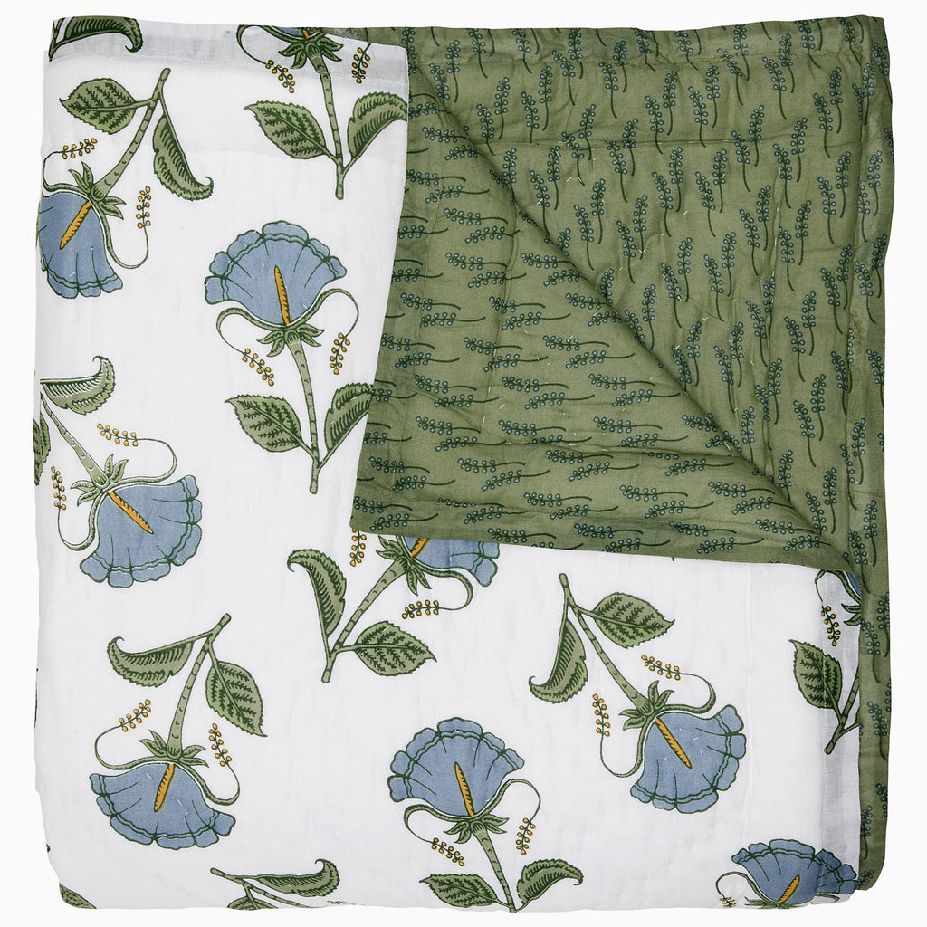 The Farah Light Indigo Bedding Collection by John Robshaw features a hand-quilted cotton voile quilt with one white side decorated with indigo and green floral motifs, and a reversed green side displaying a subtle, leaf-like pattern.