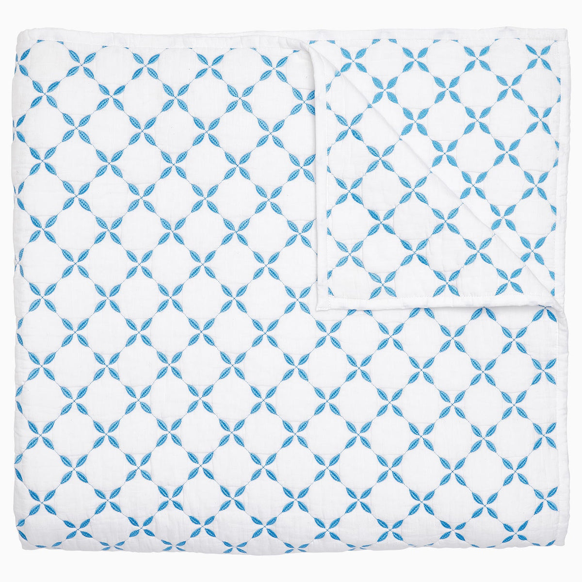 The Layla Bedding Collection by John Robshaw showcases a white cotton voile quilt adorned with a repeating blue geometric pattern of interlocking circles, neatly folded to reveal its reverse side, echoing the intricate motifs inspired by Mughal gardens.