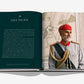 The open book, "Raffles" by Assouline, features a section titled "Asia Pacific" on the left page with insights about India and Afghanistan. The right page showcases Asian charm with a painting of a man in a red hat and ornate military uniform echoing British refinement.