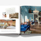An open Raffles book by Assouline unveils a luxurious blue-themed decor with a grand chandelier and plush seating reflecting British refinement. Smaller inset images display a pink-themed bedroom and a note with text.