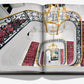 An open book displaying an ornate spiral staircase with red patterned carpet runners and intricate railing designs, viewed from above. A grand chandelier, reminiscent of the opulence found in a luxury hotel like the Ritz Paris, is also visible in the stairwell space. The book shown is "Eternally Ritz" by Assouline.