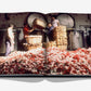 Inside an industrial facility, four people handle baskets among piles of red and white flowers—illustrating the journey of natural ingredients in Robertet: From Seed to Scent, a book by Assouline.