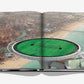 An aerial view of a tennis court on a helipad, showcasing two players against the breathtaking backdrop of a coastal city and beach, evokes scenes from "Federer" by Assouline—a tribute to the tennis legend's elevated career.