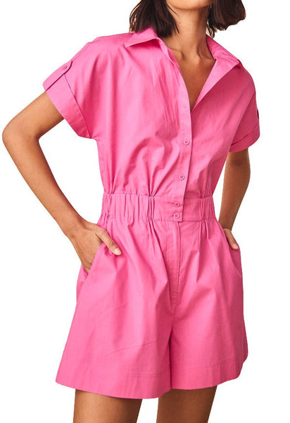 Woman in a pink cotton poplin short-sleeve Hunter Bell NYC Reed Jumpsuit with buttons and a waist-tie detail.