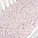 The Gooselings Dreaming of Paradise Crib Sheet is a light pink cotton sateen sheet with a delicate floral and bird pattern, OEKO-TEX certified for peace of mind.