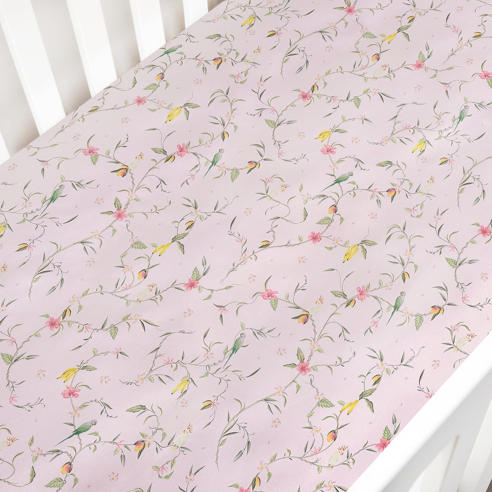 The Gooselings Dreaming of Paradise Crib Sheet is a light pink cotton sateen sheet with a delicate floral and bird pattern, OEKO-TEX certified for peace of mind.