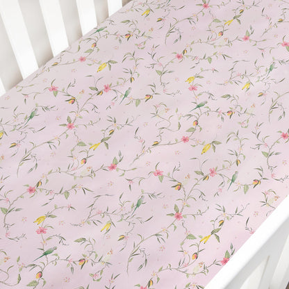 The Gooselings Dreaming of Paradise Crib Sheet is a light pink cotton sateen sheet with a delicate floral and bird pattern, OEKO-TEX certified for peace of mind.