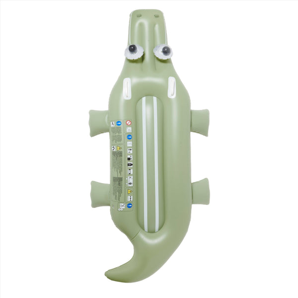 Inflatable green swimming pool float shaped like a crocodile with googly eyes and safety instructions printed on its side, perfect for a poolside adventure. Introducing Sunnylife Lie-On Float, Cookie the Croc Khaki for endless fun!
