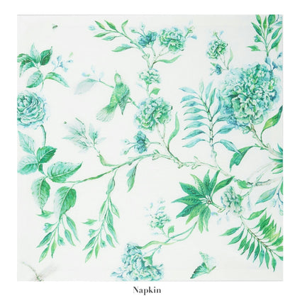The Secret Garden Table Linen Collection napkin by Aquazzura Casa features a white base with green and blue floral and bird prints, ideal for pairing with matching tablecloths or placemats to create a charming tablescape.