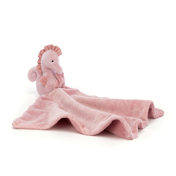 A coral-pink Sienna Seahorse stuffed animal lying on a blanket by Jellycat.