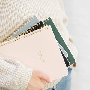 A person wears a cream sweater and blue jeans while holding several colorful spiral notebooks, with the top one—the Sugar Paper "Mom/Life" Spiral Notebook—featuring "MOM LIFE" elegantly stamped in gold. This chic notebook is perfect as an organized mom notebook or a guided planner for moms.