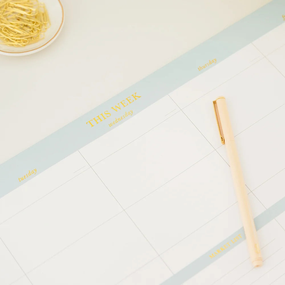 The Sugar Paper Desktop Family Planning Pad is a large-format weekly planner with spacious blank sections, accompanied by a gold pen and a dish of gold paper clips in the corner. Ideal for organizing your schedule, this pad also includes space for a daily menu section to help you keep track of meals throughout the week.