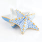 The Herend Starfish Box Collection features a star-shaped ceramic box with a removable lid, adorned with hand-painted blue and gold geometric designs and gold dots on a white background.