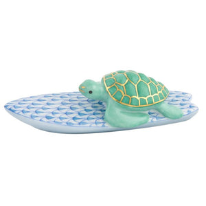 The Herend Surfing Turtle features a blue patterned ceramic base topped with a green turtle figurine accented in gold, creating a timeless decorative accent for any space.