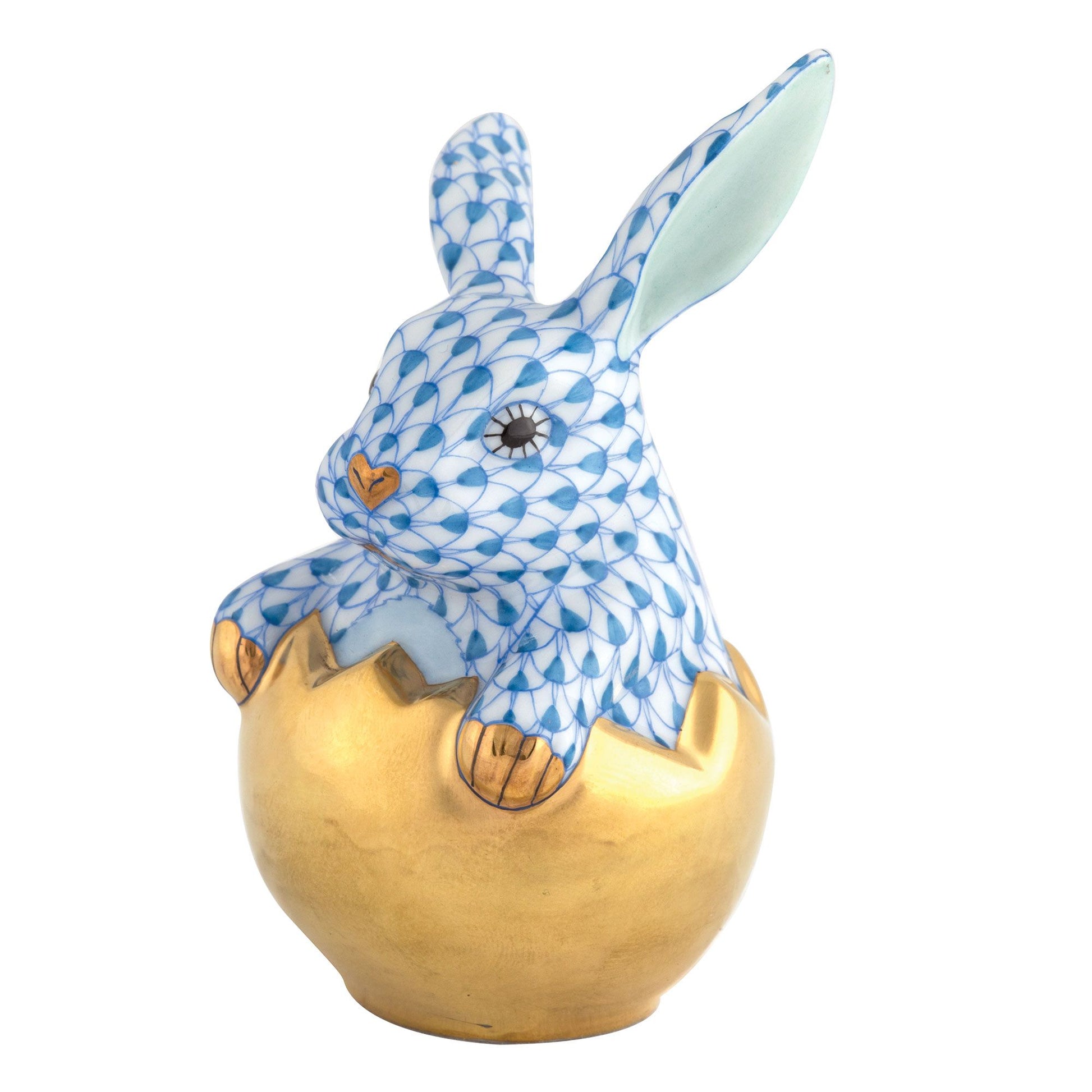 The Herend Hatching Bunny is a blue and white porcelain rabbit with gold accents, emerging from a metallic gold eggshell, featuring exquisite hand-painted designs.