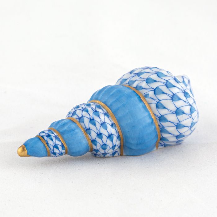 The Herend Staircase Shell Collection features a ceramic seashell figurine with a blue and white fish scale pattern and gold accents, inspired by hand painted designs, displayed on a plain white surface.