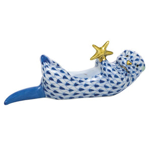 The Herend Sea Otter With Starfish is a hand-painted porcelain figurine featuring a blue and white patterned otter lying on its back holding a yellow starfish, perfect as a charming decorative accent.